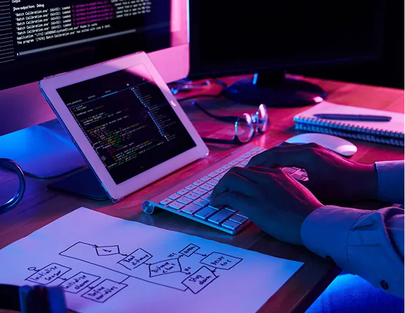 A tablet showing code on a desk lit in pink and blue