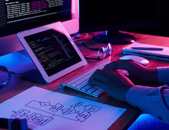A tablet showing code on a desk lit in pink and blue