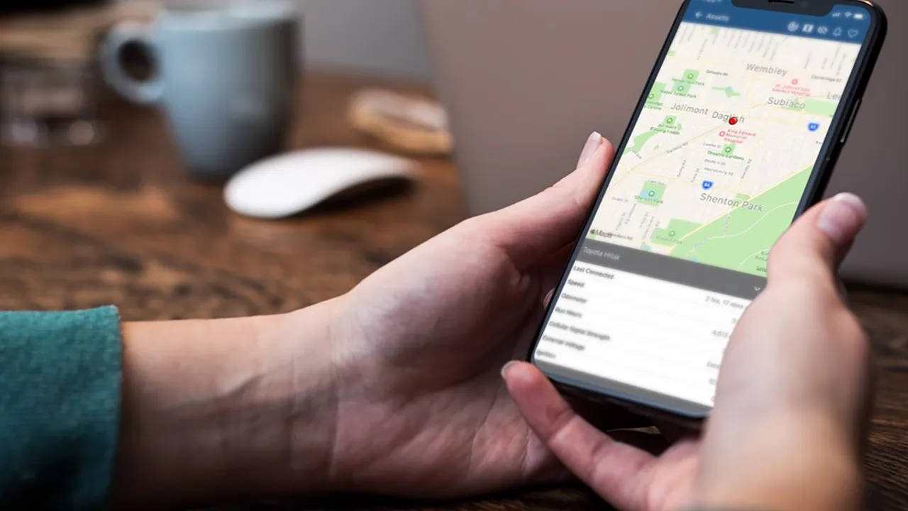 A hand holding a phone showing the Telematics Guru app map