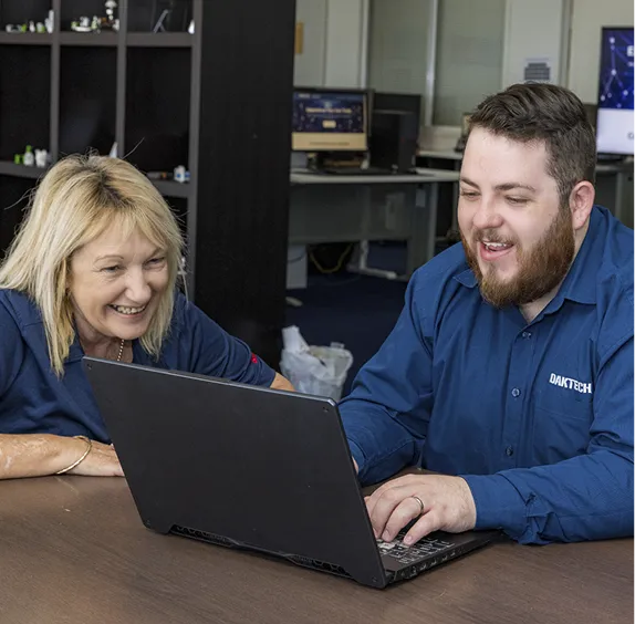 Two DakTech team members laughing together at a laptop in the office